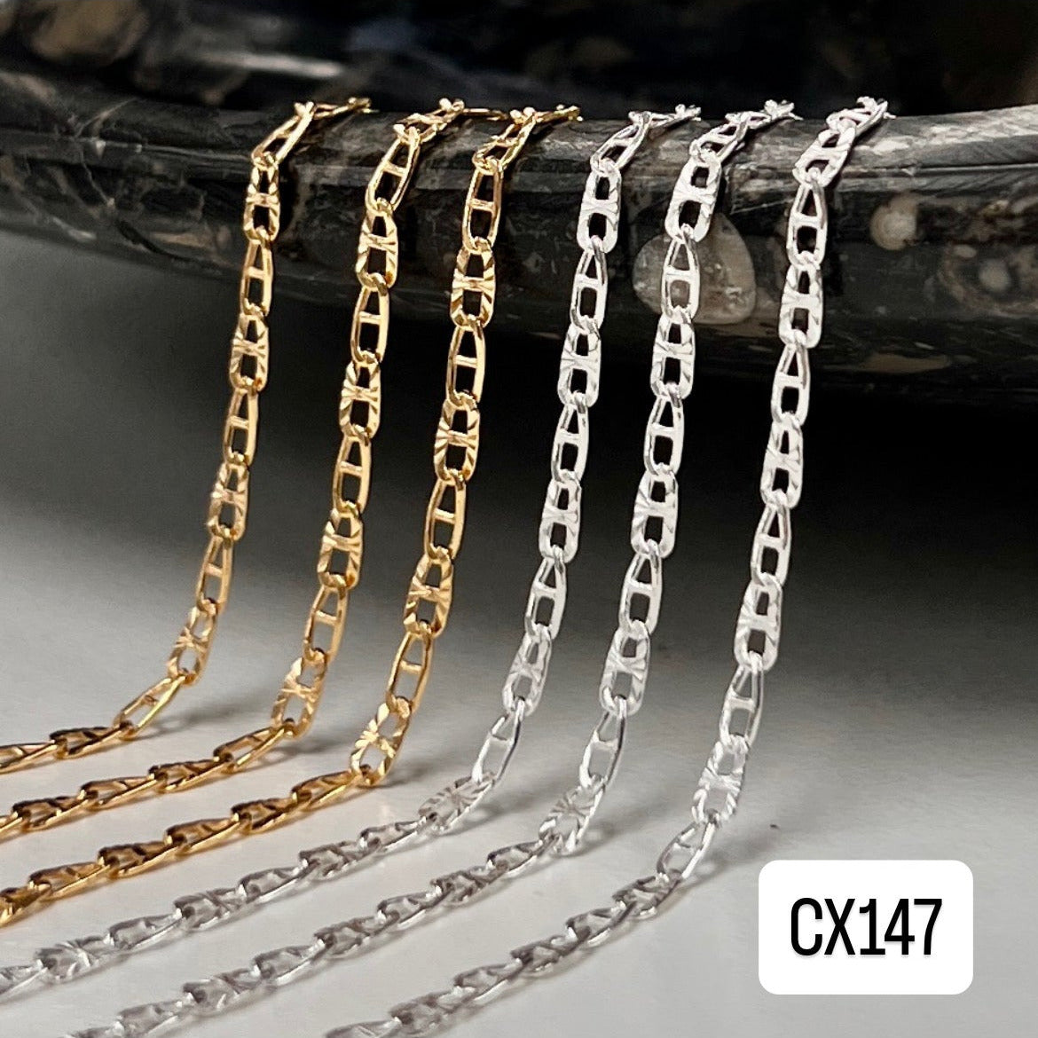 Gold and silver chain necklaces on a dark surface with 'CX147' label.