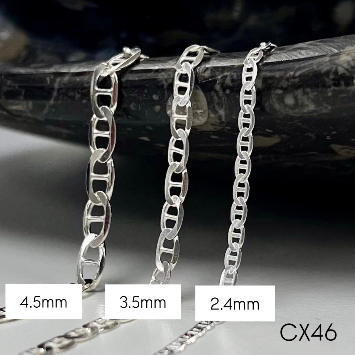 Three silver mariner chain necklaces of different widths on a dark background